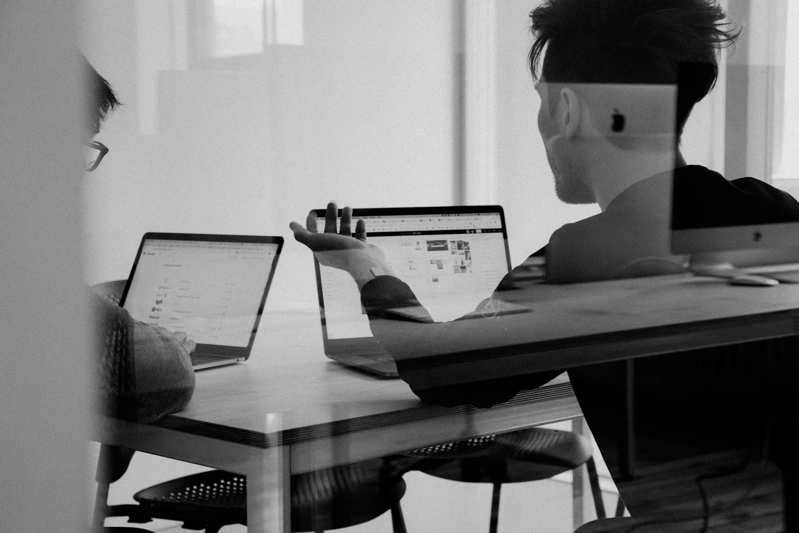 Two people discussing work across laptops at a table